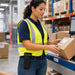 Worker wearing an Agoz wireless scanner mountable case on a waist belt while handling a labeled package at a warehouse workstation.
