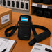 Black Agoz shoulder sling case with Almex mobile computer staged on a packing workstation with SKU labels, pick list, barcode sheets, and shipping supplies.