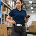 Warehouse employee wearing an Agoz utility apron while holding an Almex mobile computer for inventory and fulfillment work