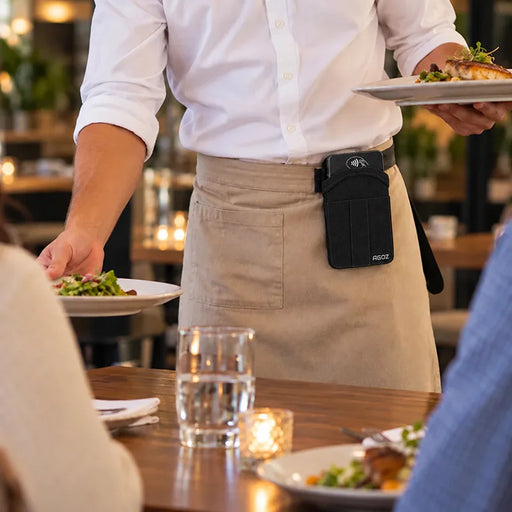 Restaurant server wearing an Agoz rugged Castles POS holster on the waist while serving food, showing convenient hands-free access during table service.