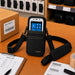 Black Panasonic Toughbook shoulder sling holster with device displayed in pouch on a retail packing workstation.