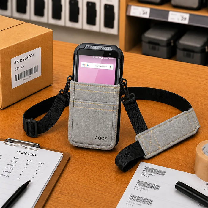Gray AgozTech Point Mobile crossbody holster with Point Mobile handheld device displayed on a warehouse packing desk with a clipboard, barcode labels, tape roll, and shipping box in the background.