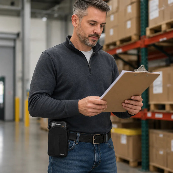 Warehouse employee reviewing inventory paperwork while wearing a black AGOZ belt case holding a rugged Chainway handheld scanner.