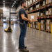 Warehouse employee with Janam rugged mobile computer in a holster is carrying packages in a warehouse