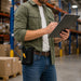Warehouse employee reviewing inventory on a clipboard while wearing a black AGOZ belt holster holding a Chainway handheld scanner in a storage aisle.