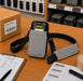 Gray Cognex barcode reader sling holster staged on a warehouse workstation with barcode labels, pick list, and packing supplies.