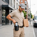 Delivery worker using a leather Panasonic Toughbook scanner case on a belt while carrying a package during field delivery work.