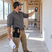 Construction professional measuring an interior wall with a Makita laser distance measure while wearing an Agoz utility tool pouch on his waist belt.