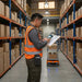 Warehouse worker wearing an AgozTech scanner case with front credential slot while reviewing a clipboard and using a handheld mobile computer in an inventory aisle.