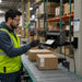 Warehouse worker pulling a printed shipping label from a TSC desktop label printer mounted on an AgozTech black wall mount shelf near a conveyor line.