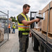 Worker wearing an Agoz belt-mounted scanner case scans a pallet label with a Bluebird trigger-handle scanner during loading and logistics operations.
