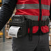 Close-up of an AgozTech Zebra ZQ521 printer waist belt carrying case worn by a warehouse worker in a red safety vest, with a label printing in use.